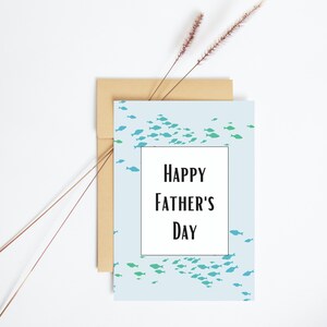 May include: A light blue card with a school of blue and green fish printed on it. The card has a white rectangle in the center with the text "HAPPY FATHER'S DAY" in black.