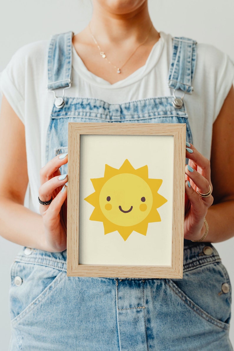 Puede incluir: Una impresi&oacute;n enmarcada de un sol amarillo de dibujos animados con una cara sonriente. El sol tiene una cara amarilla con dos peque&ntilde;as mejillas rojas y una sonrisa con la boca cerrada.