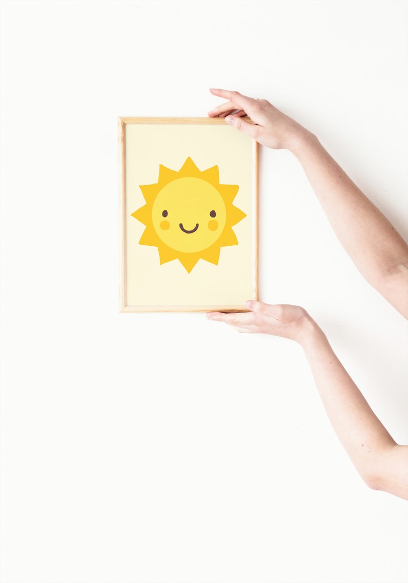 Puede incluir: Una impresi&oacute;n enmarcada de un sol amarillo de dibujos animados con una cara sonriente. El sol tiene un fondo amarillo claro y est&aacute; enmarcado en un marco de madera claro.