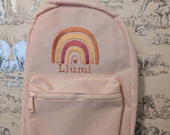 May include: A pink canvas backpack with a rainbow embroidered design and the name "Llumi" embroidered below.