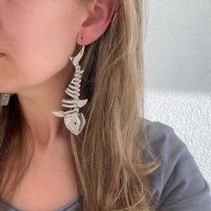 May include: A pair of white skeleton shark earrings. The earrings are dangling and feature a detailed shark skeleton design.