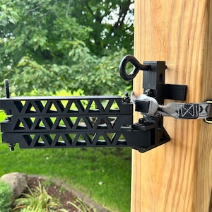 May include: Black archery target stand with a triangular design, mounted to a wooden post. The stand has a metal ring and a strap with the text "Hunt From Above."