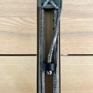 May include: A close-up of a gray and black rope secured to a metal pole with a gray plastic clip labeled "SKELETON".