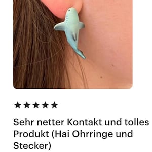 K&ouml;nnte beinhalten: Ein hellblauer Ohrring in Form eines Hais wird im Ohr gezeigt. Der Ohrring ist ein Stecker. Das Bild zeigt auch das Ohr und einen Teil des Gesichts der Person, die den Ohrring tr&auml;gt.