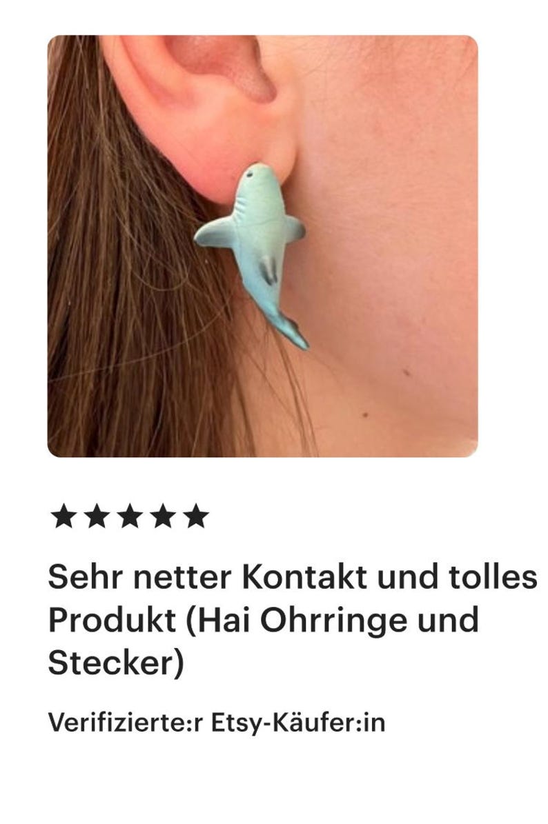 K&ouml;nnte beinhalten: Ein hellblauer Ohrring in Form eines Hais wird im Ohr gezeigt. Der Ohrring ist ein Stecker. Das Bild zeigt auch das Ohr und einen Teil des Gesichts der Person, die den Ohrring tr&auml;gt.