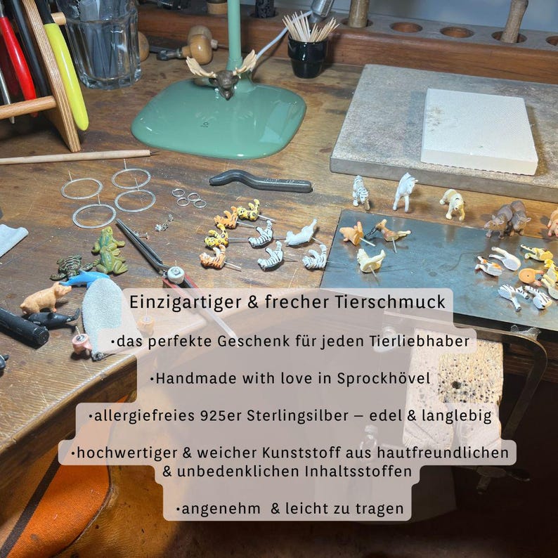 K&ouml;nnte beinhalten: Eine Sammlung von Miniatur-Tierfiguren, darunter Zebras, Tiger und andere Wildtiere, ist auf einer Holzoberfl&auml;che angeordnet. Das Bild zeigt auch Werkzeuge und Materialien zur Schmuckherstellung, was auf ein handgefertigtes Schmuckthema hindeutet.