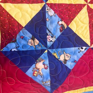 May include: A blue and yellow patchwork quilt with a farm animal print. The quilt is made of squares and triangles and features a variety of animals, including a cow, a pig, a chicken, and a cat. The quilt is quilted with a swirling pattern.