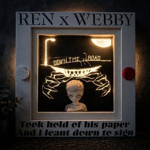 May include: A square, white-framed shadow box with internal lighting featuring the text REN x WEBBY at the top and DOWN THE ROAD in the centre. A sculpted figure of a person stands below a glowing, clawed creature, with the text Took hold of his paper And I leant down to sign at the bottom. A small white circular accent is on the left and a red circular accent is on the right.