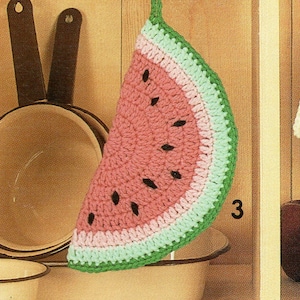 Może przedstawiać: Hakowana ściereczka w kształcie arbuza wisząca na drewnianych drzwiach szafki. Ściereczka jest zielona, różowa i biała z czarnymi pestkami. Na drzwiach szafki widnieje liczba "3".