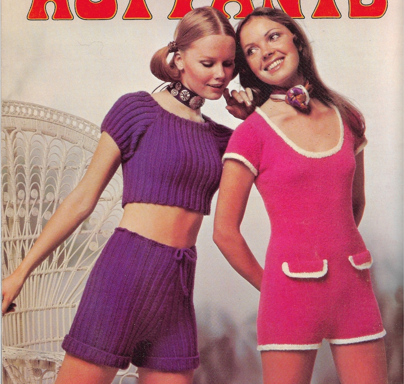 May include: Two women modeling knitted clothing. The woman on the left is wearing a purple crop top and matching shorts. The woman on the right is wearing a pink knitted dress with white trim. Both women are wearing necklaces.