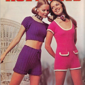 May include: Two women modeling knitted shorts and a jumpsuit. The woman on the left is wearing a purple knitted crop top and matching shorts. The woman on the right is wearing a pink knitted jumpsuit with white trim. The image is from a vintage knitting pattern leaflet.