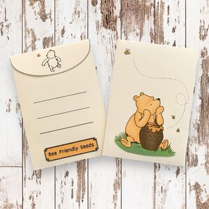 May include: A Winnie the Pooh themed envelope with a pocket on the front. The envelope is cream coloured with brown lines and the text "Bee Friendly Seeds". The back of the envelope features a cartoon image of Winnie the Pooh sitting next to a pot of honey with bees flying around him.