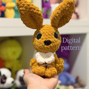 May include: A crocheted mustard-yellow bunny with large ears, black eyes, and a white collar. The text "Baby bunny" is above the bunny, and "Digital pattern" is below it. The bunny is held in a hand.