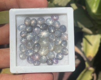 May include: A white box filled with a collection of oval-shaped, light blue star sapphires.