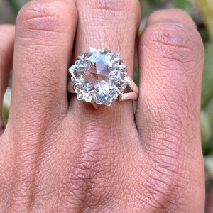 Puede incluir: Un anillo de plata con una gran piedra preciosa de cuarzo facetado transparente. La piedra preciosa está tallada en forma de estrella.
