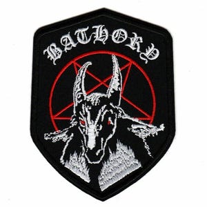 以下が含まれることがあります： 黒い背景の盾形の刺繍ワッペン。上部にアーチ状の白い「BATHORY」の文字、中央に赤い五芒星、その上に赤い目をした白いヤギの頭のイラストがデザインされています。