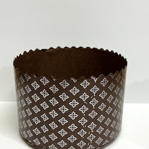 Könnte beinhalten: Eine braune Papierbackform mit einem weißen Blumenmuster. Die Form ist zum Backen eines Kuchens oder Brotes gedacht.