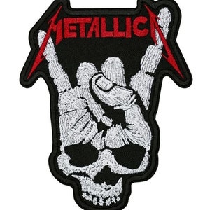 May include: Black embroidered patch with the word "METALLICA" in red, above a white skeleton hand gesture. The patch has a red lightning bolt design and a skull at the bottom. Suitable for clothing or bags.