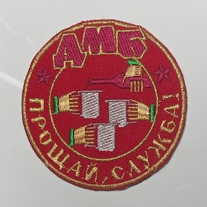 Op de afbeelding: Een rood geborduurd patch met een gouden rand. De patch heeft de tekst "AMS" in gouden letters, een gestileerde afbeelding van een fles en drie glazen, en de tekst "Прощай, Слава!" in gouden letters.
