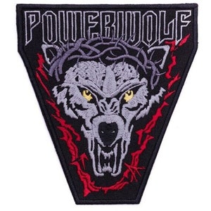 Könnte beinhalten: Schwarzer, dreieckiger Aufnäher mit dem weißen Text "POWERWOLF". Er zeigt einen detaillierten, grauen Wolfskopf mit gelben Augen und einer Dornenkrone. Rote Flammen und Akzente umgeben den Wolfskopf.