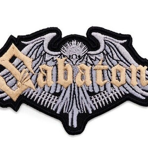 May include: Embroidered patch featuring the word "Sabaton" in a gothic font, set against a stylized winged emblem. The patch has a black border, with tan and gray detailing, suitable for jackets or bags.