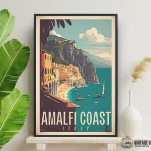 May include: A vintage travel poster featuring a colorful illustration of the Amalfi Coast in Italy. The poster has a blue background with a view of a town built into the side of a cliff overlooking a turquoise sea. The text "Amalfi Coast Italy" is printed in white at the bottom of the poster.