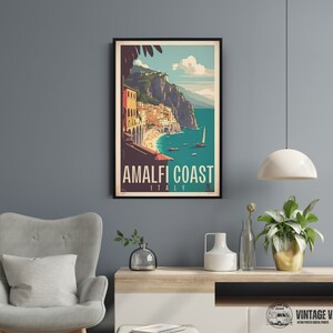 May include: A vintage travel poster featuring a colorful illustration of the Amalfi Coast in Italy. The poster has a blue background with a white sailboat and a view of the coastline with buildings and cliffs. The text on the poster reads "Amalfi Coast, Italy".