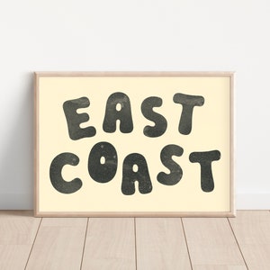 Puede incluir: Una impresi&oacute;n enmarcada con fondo crema y texto negro que dice "EAST COAST" en una fuente redonda y juguetona.