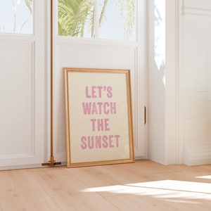 Könnte beinhalten: Ein gerahmter Druck mit einem hellbeigen Hintergrund und einer rosa Aufschrift, die "LET'S WATCH THE SUNSET" lautet.