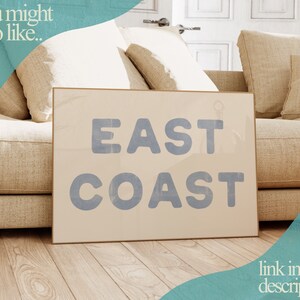 Puede incluir: Una impresi&oacute;n en lienzo beige con el texto "EAST COAST" en letras azules. La impresi&oacute;n se muestra en un sof&aacute; beige con almohadas.