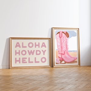 May include: Two framed prints with gold frames. The print on the left has the words "ALOHA HOWDY HELLO" in pink letters on a cream background. The print on the right shows a pair of pink cowboy boots with white embroidery on a light blue background.