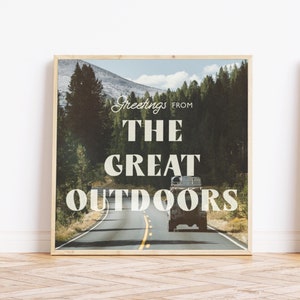 May include: A framed print with a vintage aesthetic featuring a road winding through a forest with a car driving down the road. The text "Greetings from The Great Outdoors" is printed on the image.