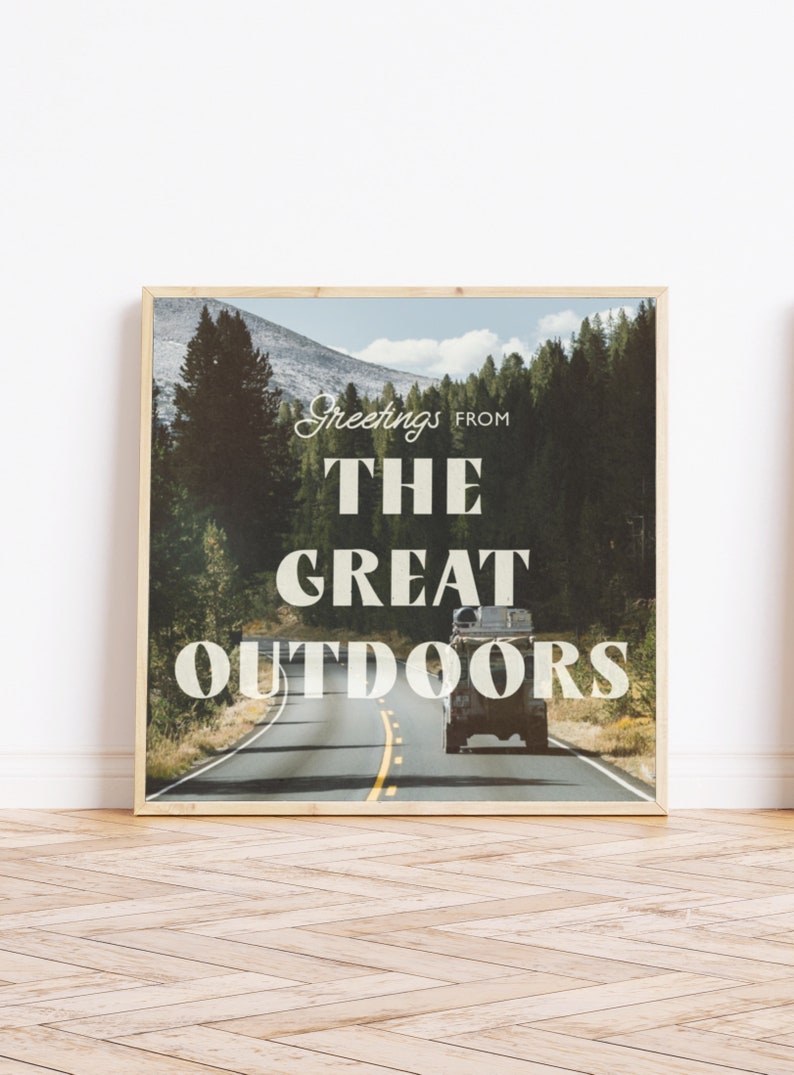 May include: A framed print with a vintage aesthetic featuring a road winding through a forest with a car driving down the road. The text "Greetings from The Great Outdoors" is printed on the image.