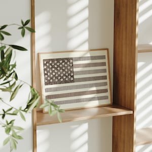 Puede incluir: Una impresión enmarcada de una bandera estadounidense con un diseño marrón y blanco en un estante de madera.
