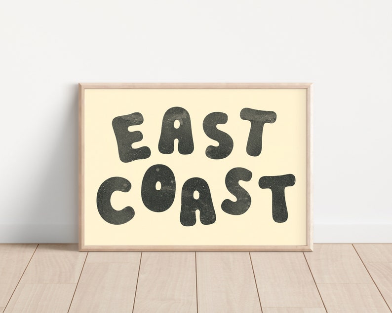 Puede incluir: Una impresi&oacute;n enmarcada con fondo crema y texto negro que dice "EAST COAST" en una fuente redonda y juguetona.