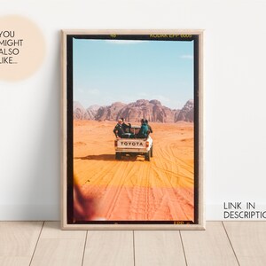 May include: A vintage photograph of a white Toyota pickup truck driving through a desert landscape. The truck is carrying three people and has a 'TOYOTA' logo on the back. The photo is framed in a wooden frame.