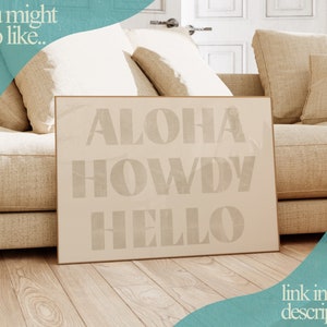 Puede incluir: Una impresi&oacute;n enmarcada beige con las palabras "ALOHA HOWDY HELLO" en una fuente blanca texturizada sobre un fondo beige.