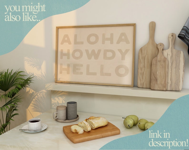 Puede incluir: Una impresi&oacute;n enmarcada con el texto "ALOHA HOWDY HELLO" en color marr&oacute;n claro sobre un fondo beige. La impresi&oacute;n est&aacute; en un estante blanco con dos tablas de cortar de madera.