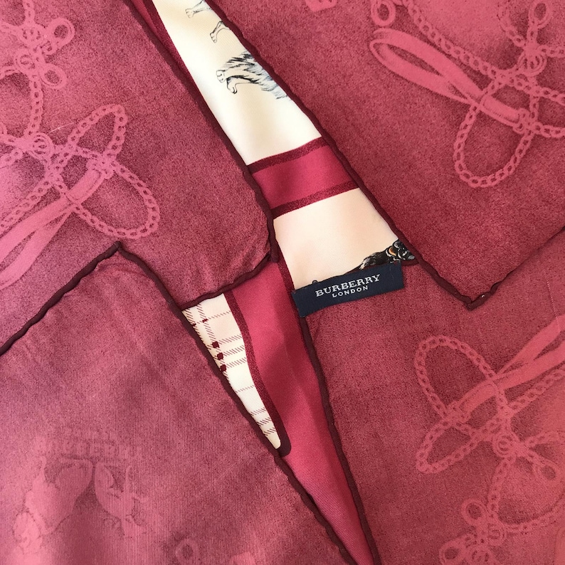May include: A collection of pink handkerchiefs with a decorative design and dark red borders. A section of a patterned scarf with the text "BURBERRY LONDON" is visible, adding a touch of luxury to the arrangement. The scarf features a cream background with horse and rider illustrations.