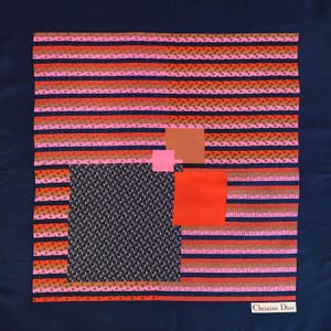 May include: A square silk scarf with a navy blue background and a geometric design. The design includes horizontal stripes in shades of pink, orange, and brown, along with squares of different colors and patterns. The words "Christian Dior" are printed in white.