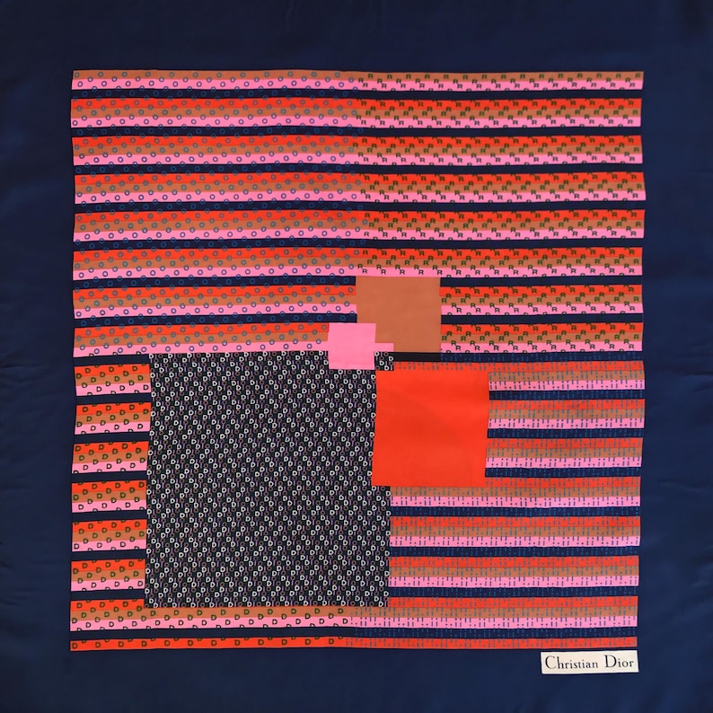 May include: A square silk scarf with a navy blue background and a geometric design. The design includes horizontal stripes in shades of pink, orange, and brown, along with squares of different colors and patterns. The words "Christian Dior" are printed in white.