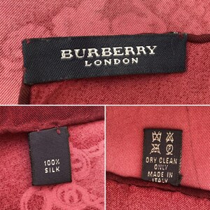 May include: Close-up of a red silk scarf with the "BURBERRY LONDON" label. The scarf is made of 100% silk and has a pattern. The care label indicates dry clean only and "MADE IN ITALY".