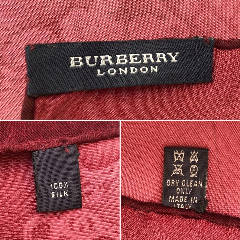 May include: Close-up of a red silk scarf with the "BURBERRY LONDON" label. The scarf is made of 100% silk and has a pattern. The care label indicates dry clean only and "MADE IN ITALY".