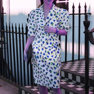 May include: A white dress with a blue floral pattern. The dress has a fitted bodice and a skirt with a slight A-line shape. The dress is made of a lightweight fabric and has a vintage style.