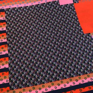 May include: A patterned textile featuring a repeating design of the letter "D" and circles in white, pink, and orange against a dark background. The design includes stripes and solid color blocks in pink, orange, and navy blue.