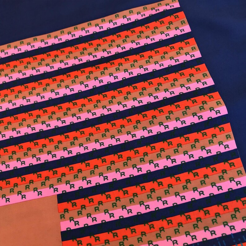May include: A patterned textile featuring rows of the letter "R" in black, arranged on stripes of red, pink, and brown. The background is a dark blue. The design is repeated across the fabric.
