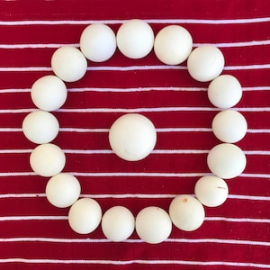 May include: A circle of white wooden balls on a red and white striped background. The balls are arranged in a circle with one ball in the center.