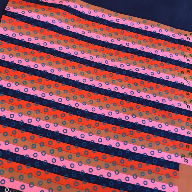 May include: A colorful patterned textile featuring diagonal stripes in navy, orange, pink, and brown. Each stripe is adorned with small blue circles. The word "DIO" is visible in the bottom left corner.