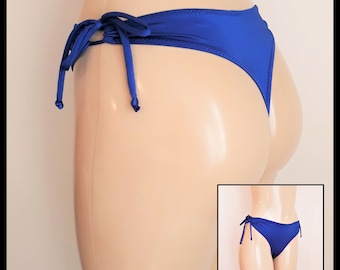 May include: A solid royal blue bikini bottom featuring side tie closures with thin fabric strings. The swimwear piece has a high-cut leg design and a smooth, matte finish, shown on a mannequin torso with an inset view of the full front.
