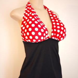 May include: A halter-style swimsuit with a red top featuring white polka dots and a solid black bottom. The swimsuit is displayed on a mannequin, showcasing its design and fit. The overall style is playful and retro.